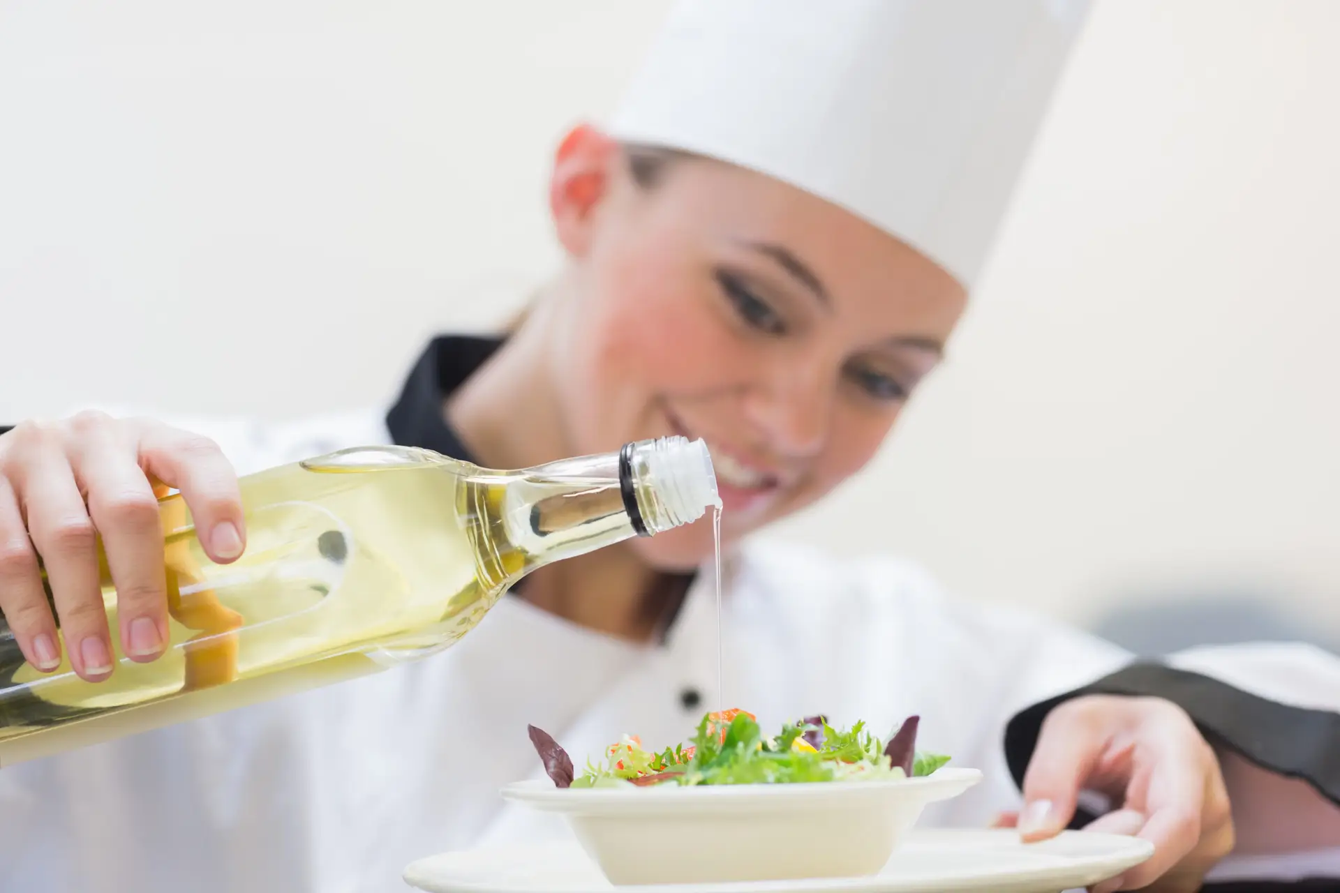 Smiling woman chef dressing a salad in the kitchen